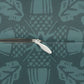 Close-up of a zipper with a white pull tab on a teal fabric background with a repeating light teal pattern.
