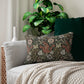 A rectangular William Morris inspired lumbar cushion with a floral pattern in beige, green, and red hues.