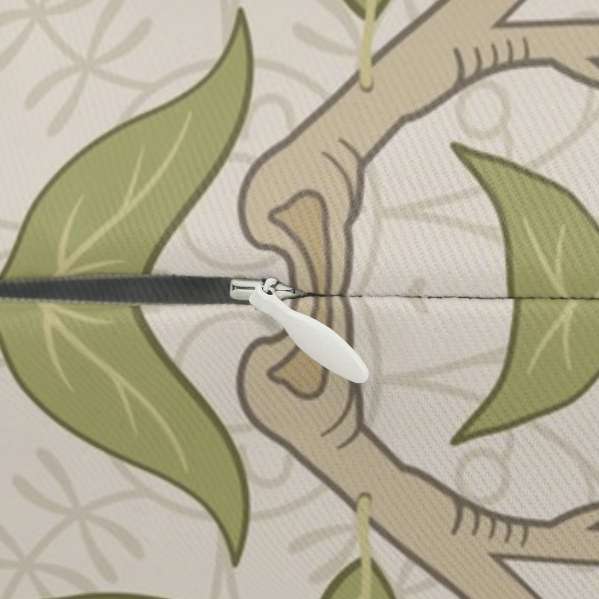 Close-up of a zipper with a white pull tab opening a fabric panel featuring a botanical pattern of green leaves and beige branches on a light cream background.