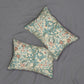 Two decorative throw pillows with a classic William Morris-style floral and scroll pattern in teal, dusty pink, and cream, arranged on a textured gray fabric background.