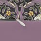 A rectangular lumbar cushion with a William Morris & Co floral pattern featuring pink and yellow flowers and green leaves on a dark background, with a concealed beige zipper.