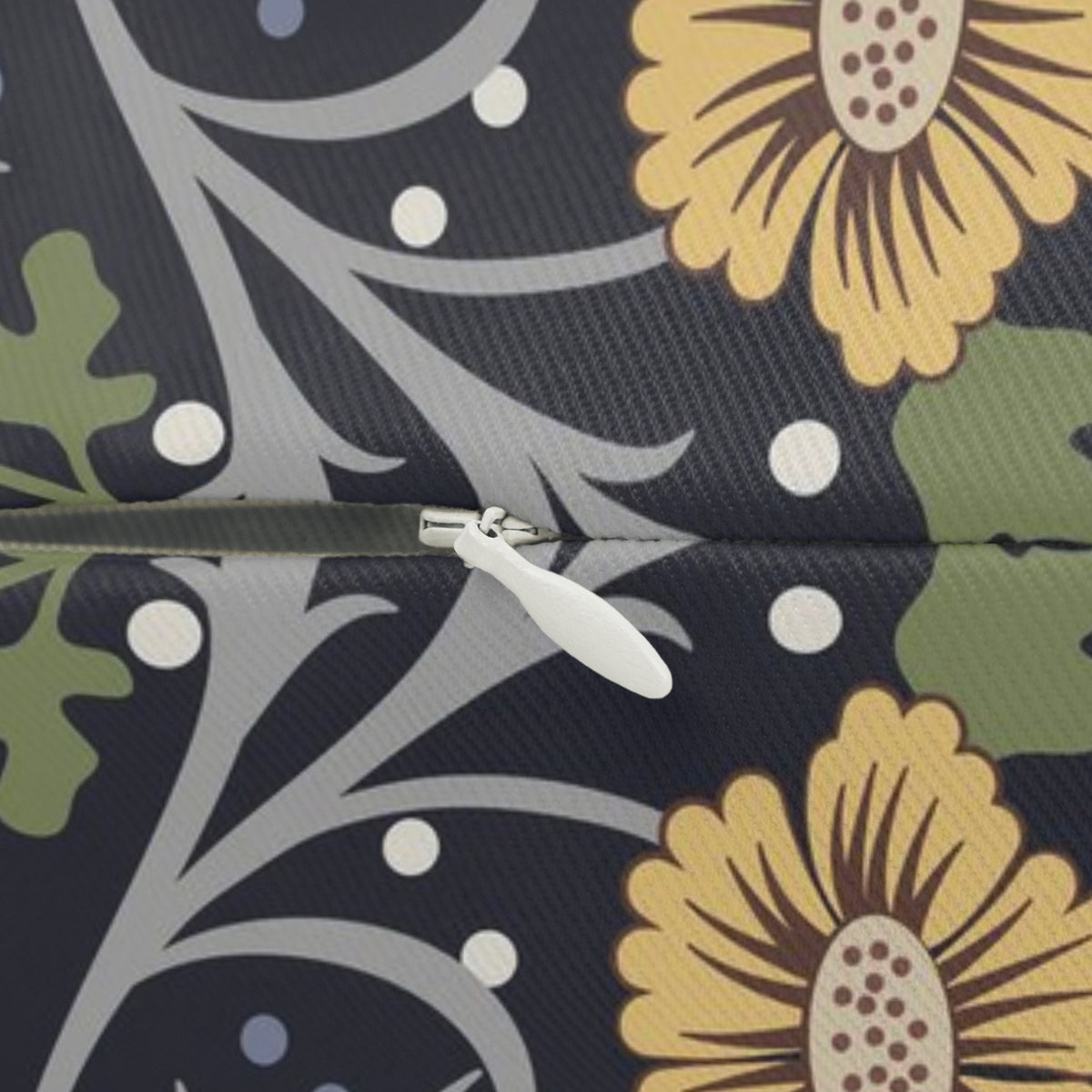 Close-up of a fabric surface with a floral and botanical pattern in dark navy, yellow, green, and gray, with a zipper running horizontally across the center.