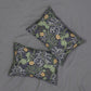 Two rectangular throw pillows with a William Morris-style floral and leaf pattern in muted green, gray, and yellow, displayed on a gray fabric background.