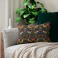 Decorative pillow with floral and bird pattern on a sofa with a plant in the background.
