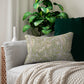Decorative pillow with green and white pattern on a couch with a plant in the background