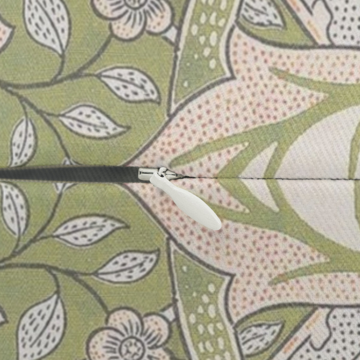 Close-up of a zipper with a white pull tab and black zipper tape, set against a patterned fabric background with green leaves and pink floral motifs.
