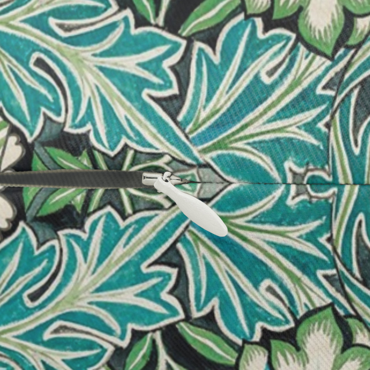 A close-up of a zipper on a fabric with a bold tropical leaf pattern in teal, green, and white.