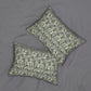 Two rectangular decorative pillows with a green and white floral pattern, arranged on a gray fabric background.