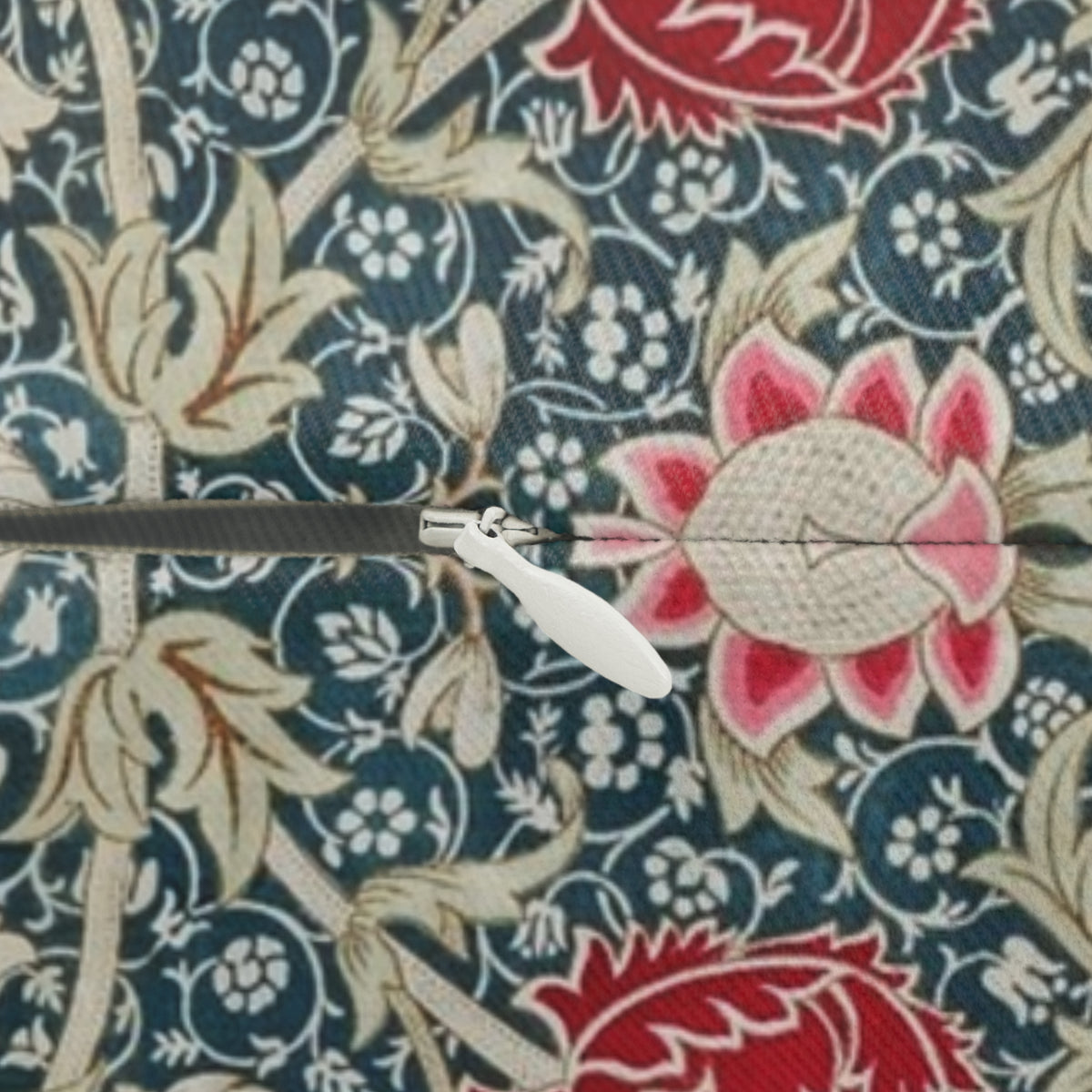 A close-up of a fabric surface with an intricate floral and botanical pattern in navy blue, beige, and red. A small white plastic hook or clip is placed horizontally across the center of the pattern.