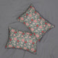 Two decorative throw pillows with a floral and bird pattern in pink, red, and cream on a blue-green background, arranged on a gray fabric surface.