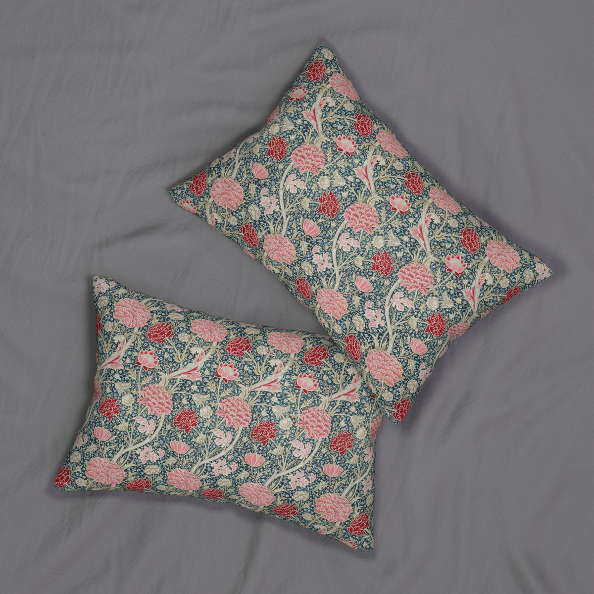 Two decorative throw pillows with a floral and bird pattern in pink, red, and cream on a blue-green background, arranged on a gray fabric surface.
