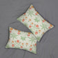 Two rectangular lumbar pillows with a green and orange botanical floral pattern on a cream background, displayed on a gray fabric surface.