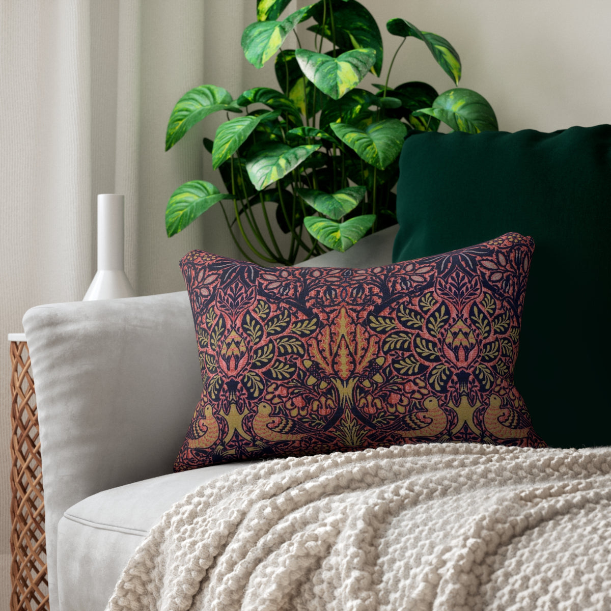 A rectangular decorative throw pillow featuring a dense, symmetrical Art Nouveau William Morris & Co pattern with stylised trees, leaves, and birds in coral pink, olive green and mustard yellow on a dark navy background.