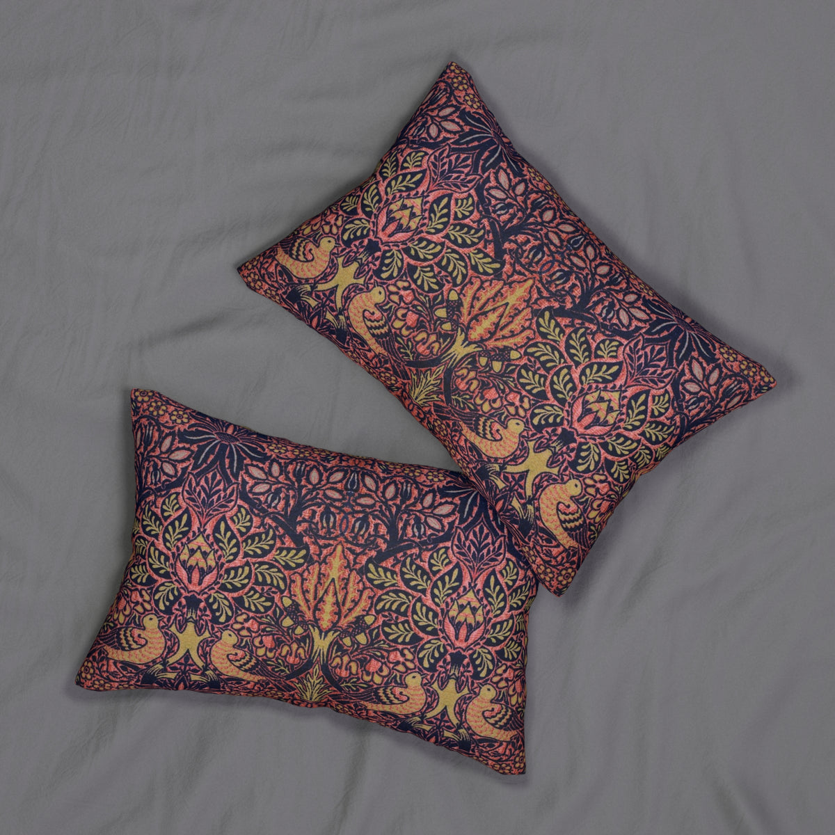 Two square decorative throw pillows with an intricate floral and bird pattern in pink, orange, green, and dark purple, arranged on a gray fabric background.