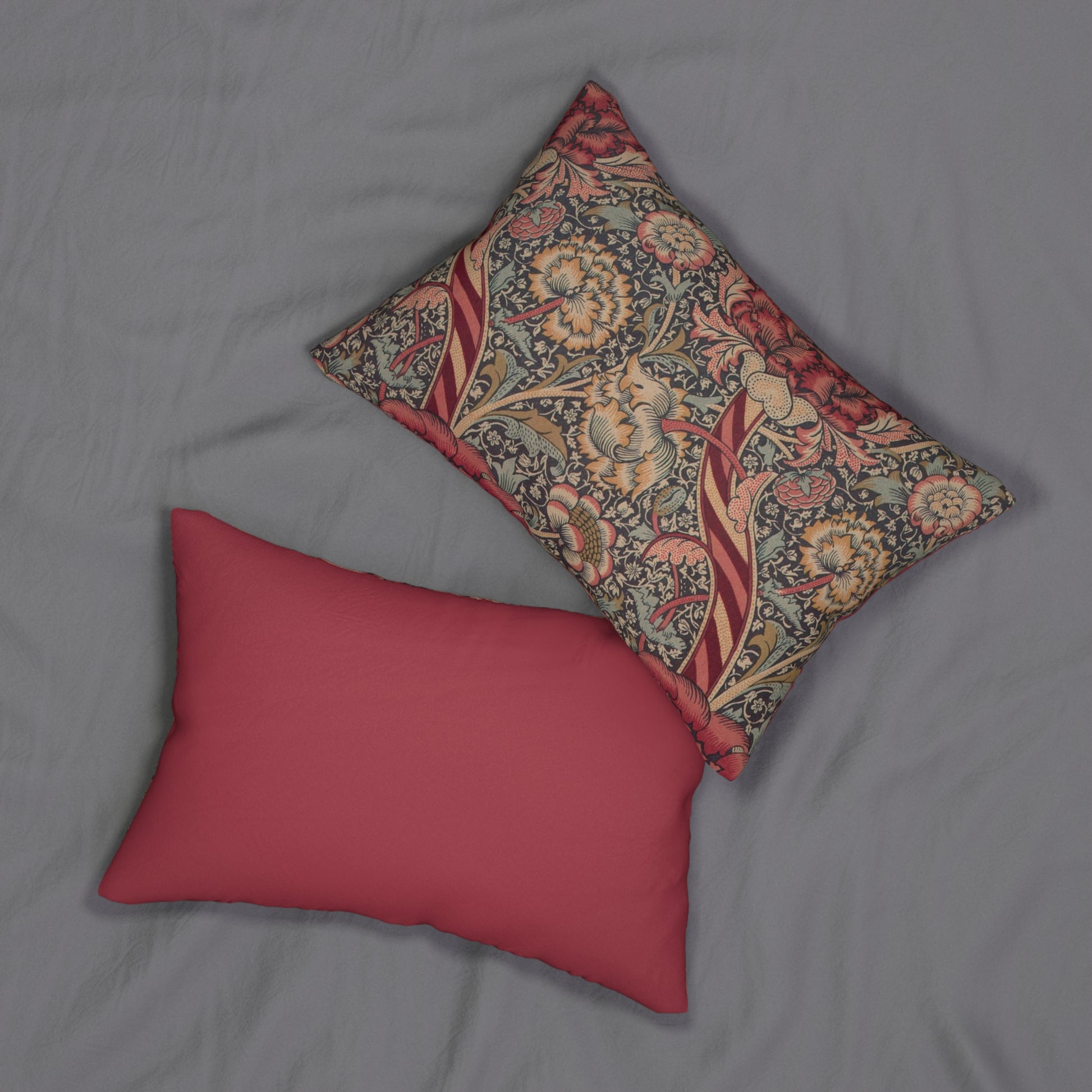 A rectangular lumbar cushion with a red and green William Morris & Co floral pattern on a textured background, featuring a concealed beige zipper.