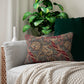 A rectangular lumbar cushion with a red and green William Morris & Co floral pattern on a textured background, featuring a concealed beige zipper.