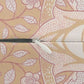 Close-up of a zipper with a white pull tab and black teeth, set against a beige and pink floral patterned fabric background.