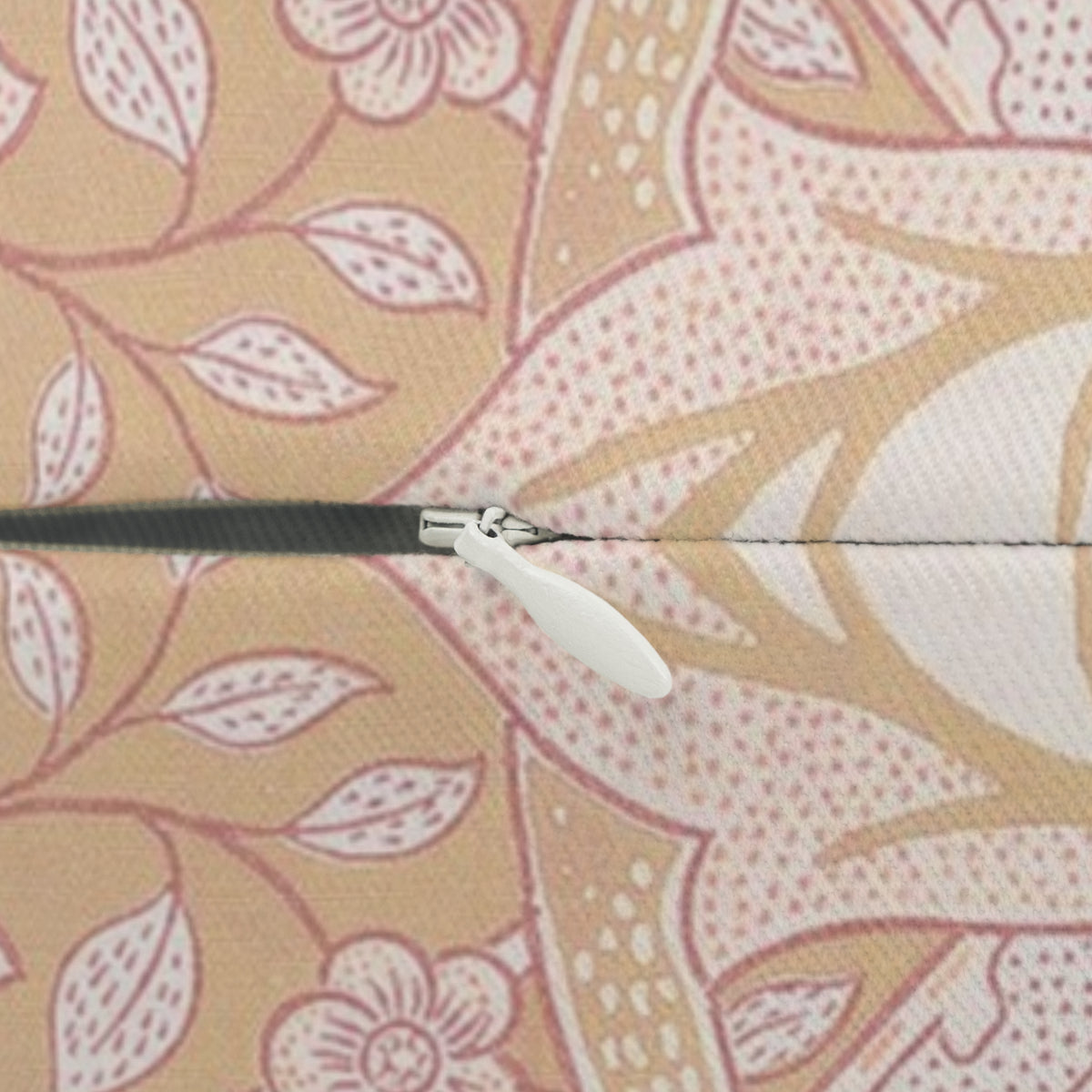 Close-up of a zipper with a white pull tab and black teeth, set against a beige and pink floral patterned fabric background.