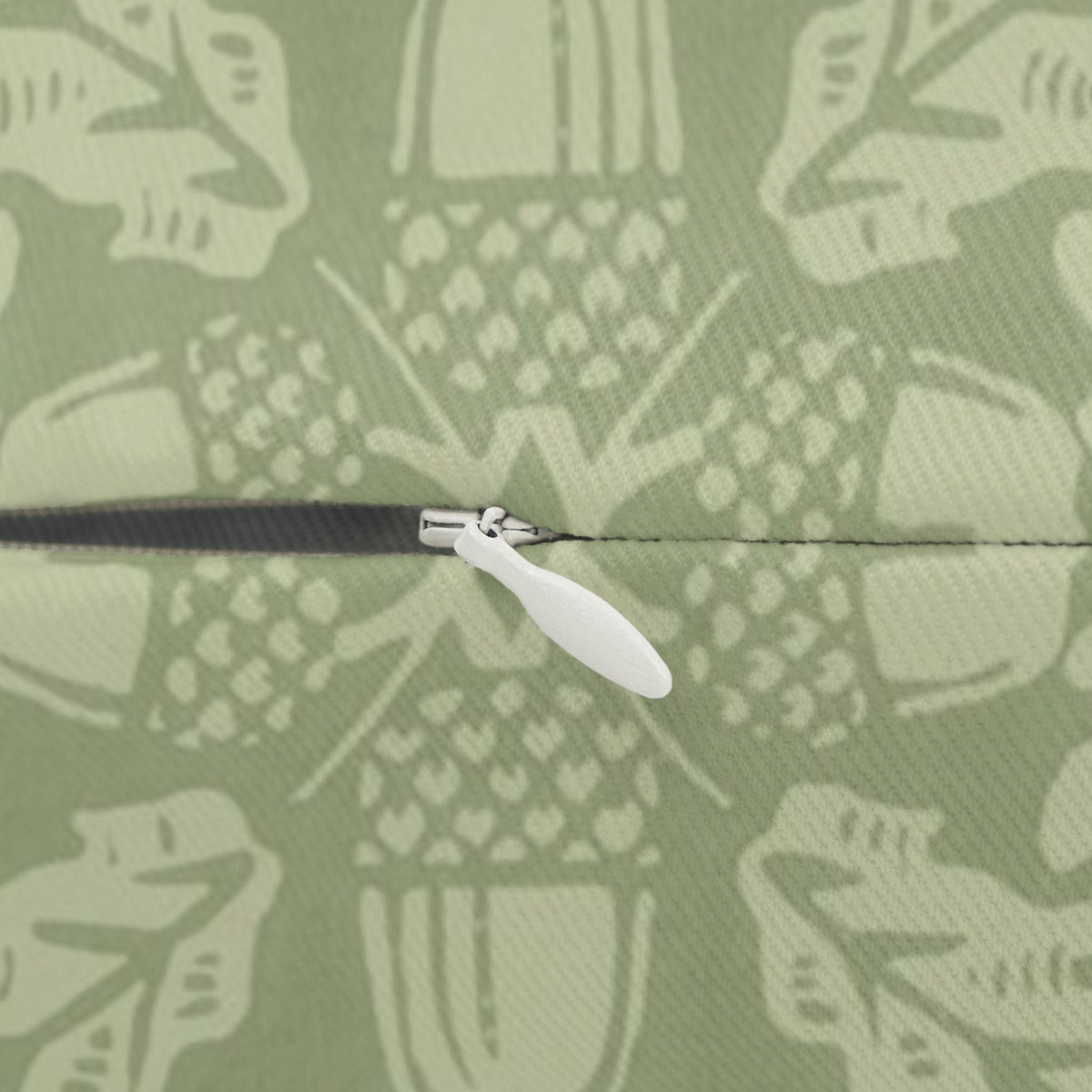 Close-up of a zipper with a white pull tab and black teeth, set against a sage green fabric background with a light cream abstract pattern.