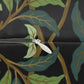 Close-up of a zipper opening a dark fabric with an allover botanical pattern of green and teal leaves, gold branches, and a black background.