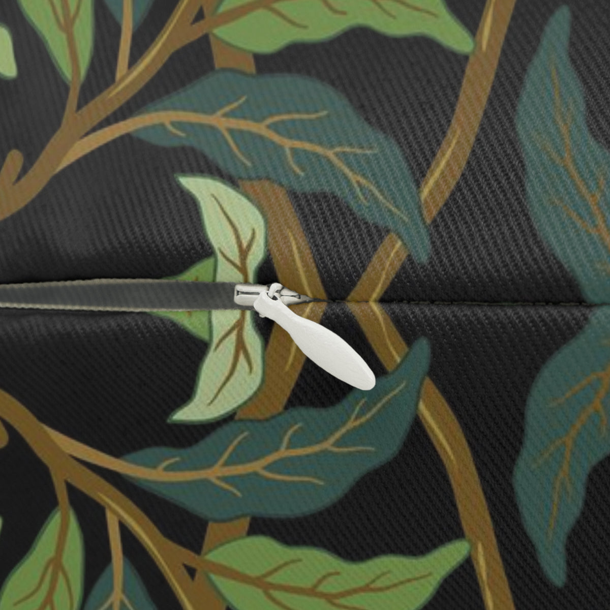 Close-up of a zipper opening a dark fabric with an allover botanical pattern of green and teal leaves, gold branches, and a black background.