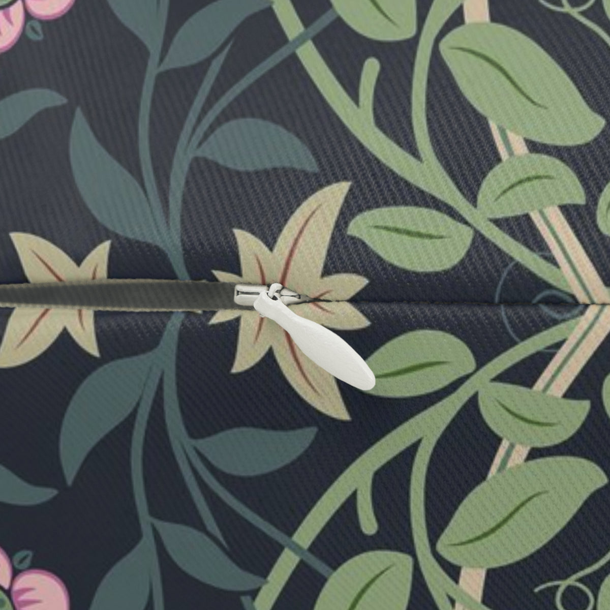 Close-up of a zipper with a white pull tab and silver metal teeth, set against a dark navy fabric printed with green leaves, beige flowers, and pink floral accents.