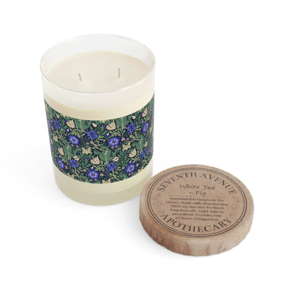 A clear glass candle with a floral patterned label and a brown wax seal on top, labeled 'Seventh Ave White Tea & Fig'.