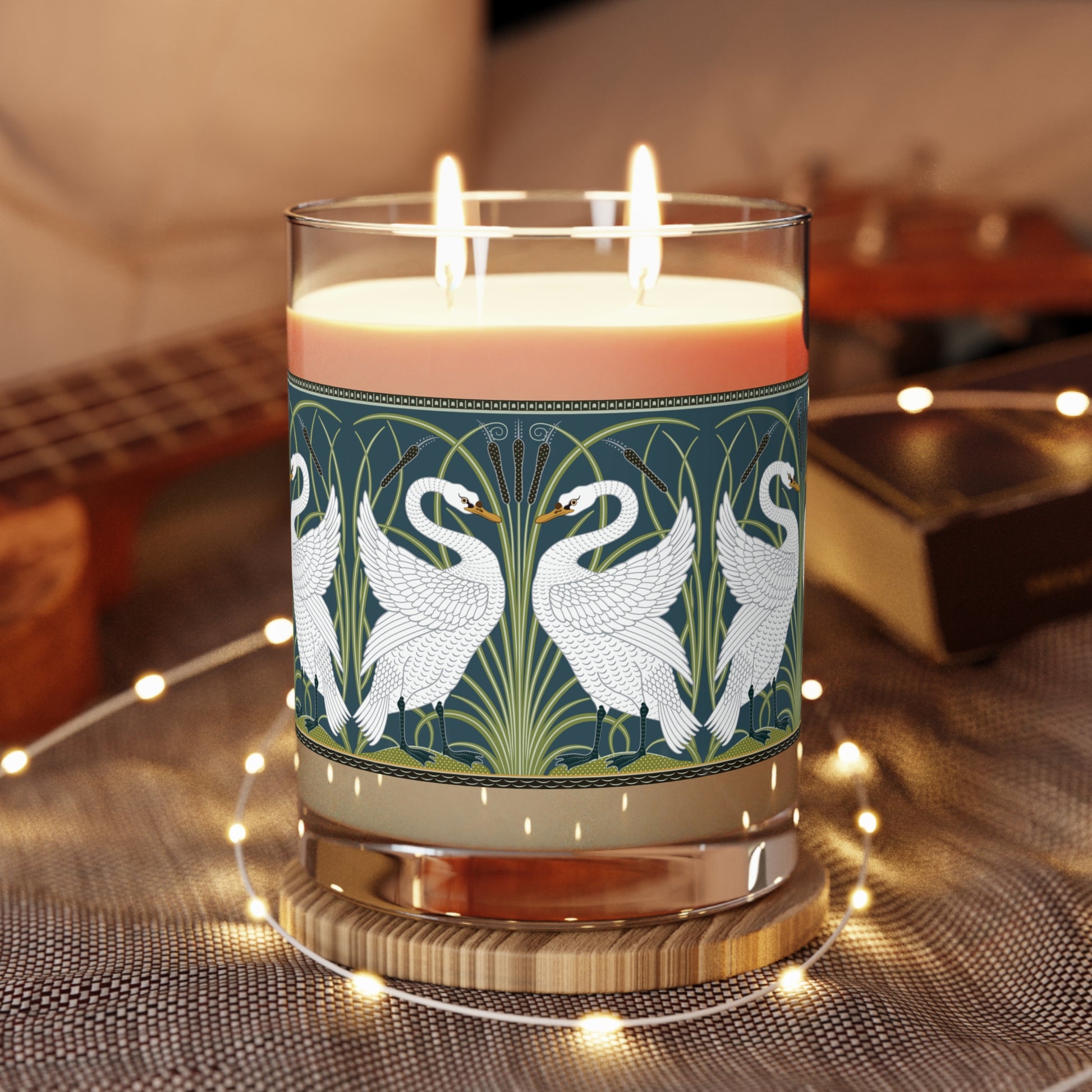A clear glass candle with a white swan design on the label, alongside a brown cardboard lid with text.