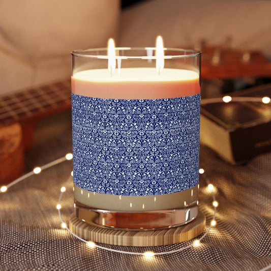 Candle with blue patterned label on a reflective surface with blurred background