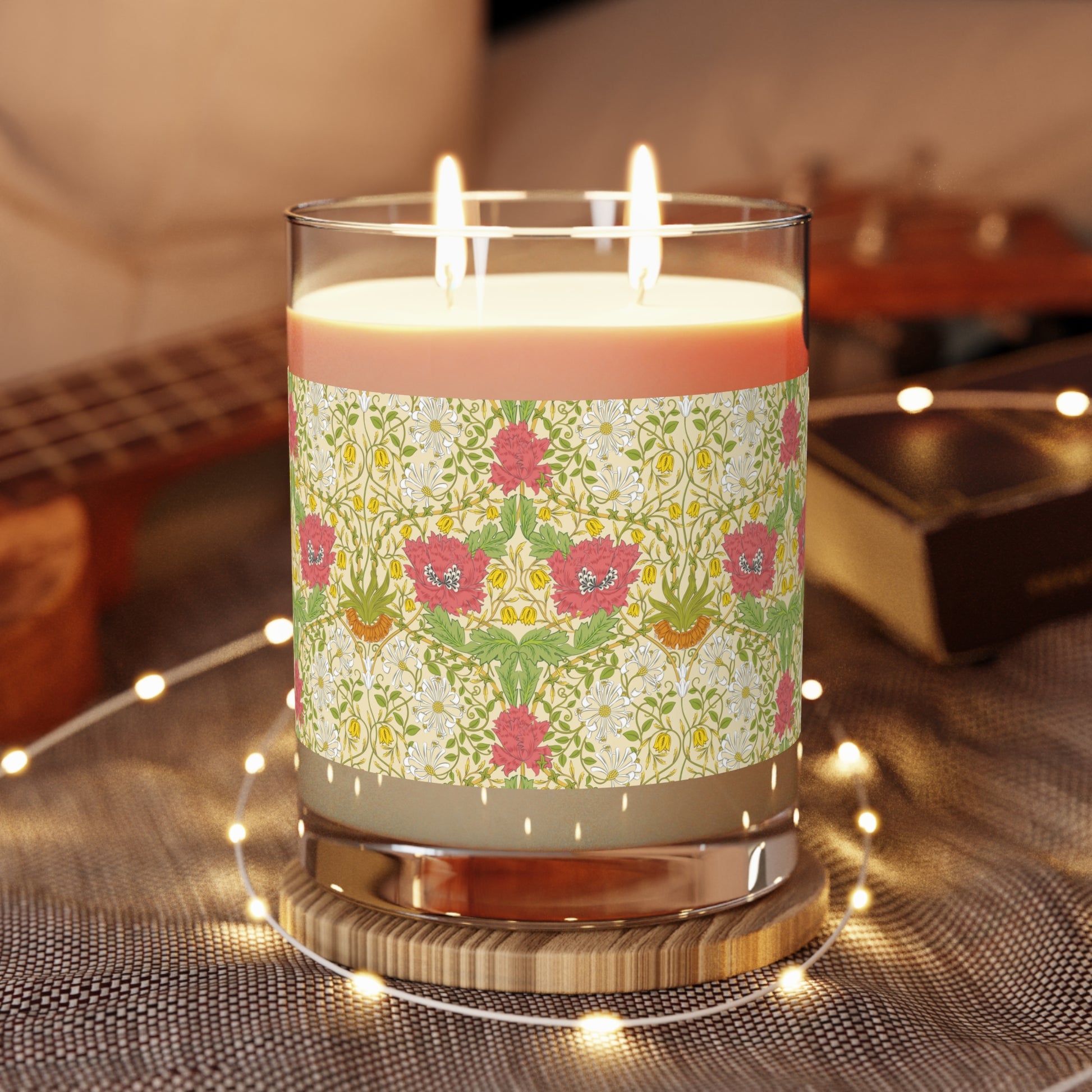 Decorative candle with floral pattern on a wooden coaster, surrounded by string lights.