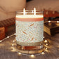 Decorative candle with a patterned label on a wooden coaster, surrounded by string lights.