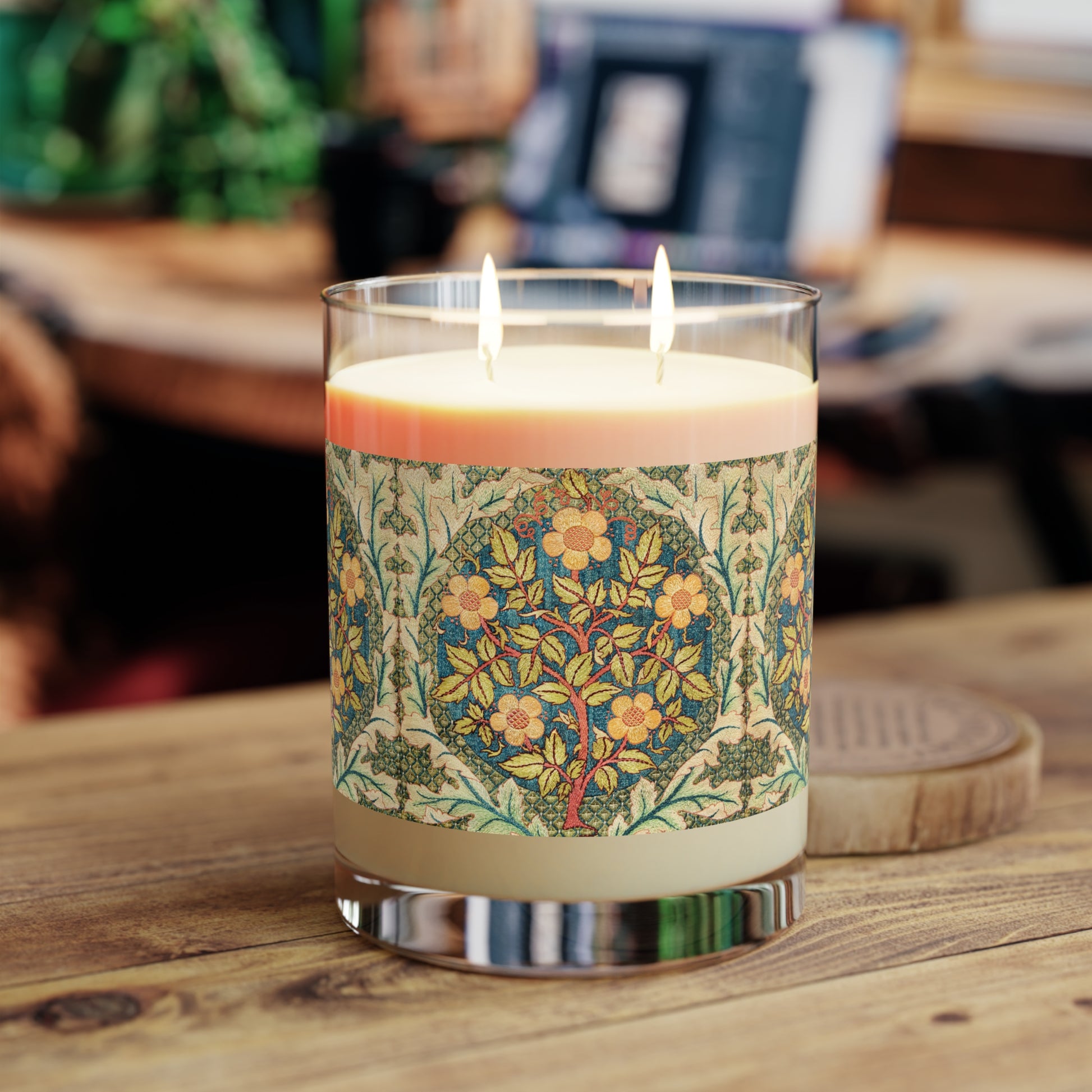 A luxury scented candle with a William Morris & Co floral pattern wrapping around the glass jar, alongside a brown cardboard lid.