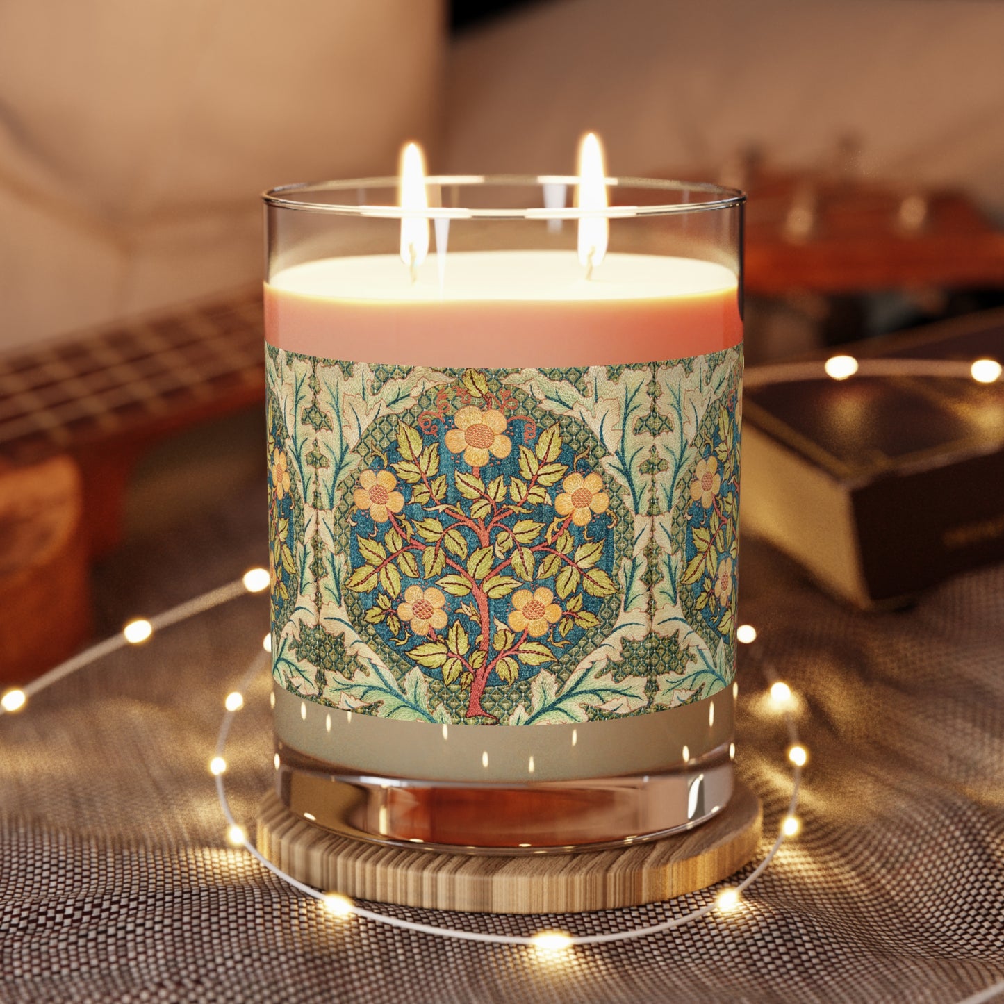 A luxury scented candle with a William Morris & Co floral pattern wrapping around the glass jar, alongside a brown cardboard lid.