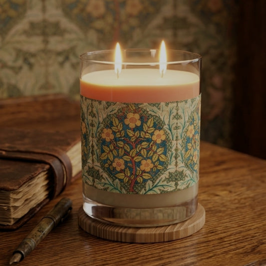 A double-wick candle in a clear glass jar with a decorative floral label, lit and set on a wooden table beside an old book and pen.
