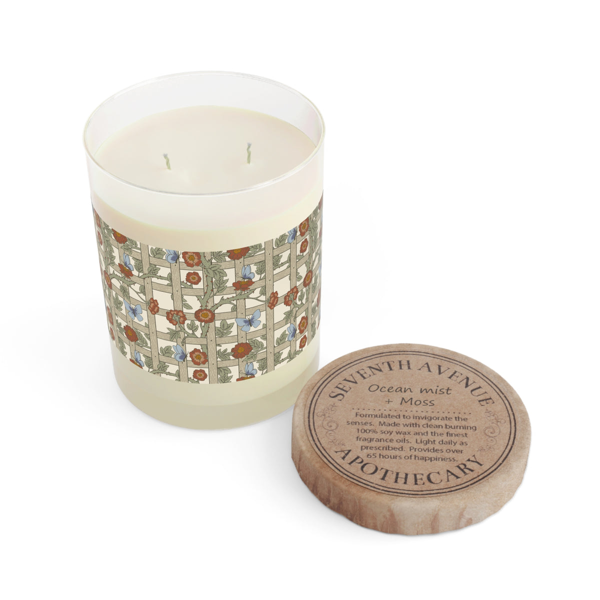 A two-wick scented candle in a clear glass vessel with cream-colored wax and a decorative botanical label, shown next to its round wooden lid on a white background. The lid is printed with the brand name 'Apothecary' and scent details.