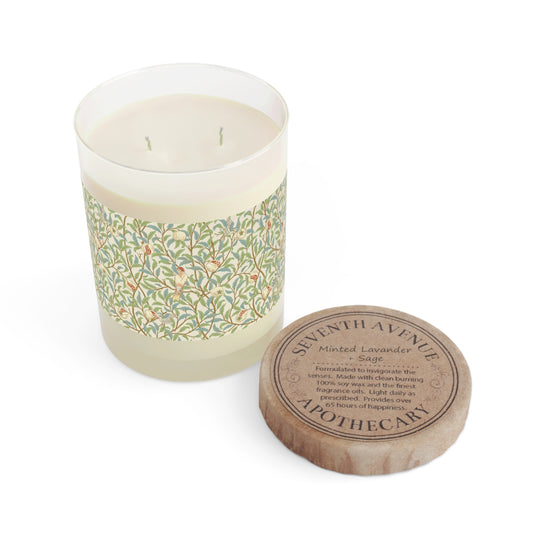 A clear glass candle with a floral patterned lid and a brown cardboard lid with the branding information on it, placed next to the candle.