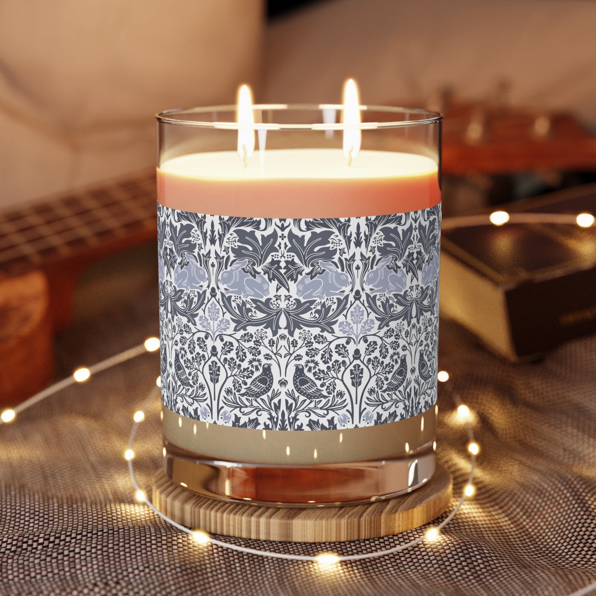 Candle with decorative label on a wooden coaster, surrounded by string lights.