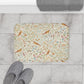 A microfibre bath mat with a floral and bird pattern inspired by William Morris, in a beige, green, and brown color palette.