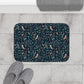 Decorative bath mat with nature-themed pattern on a tiled floor with slippers and a towel.