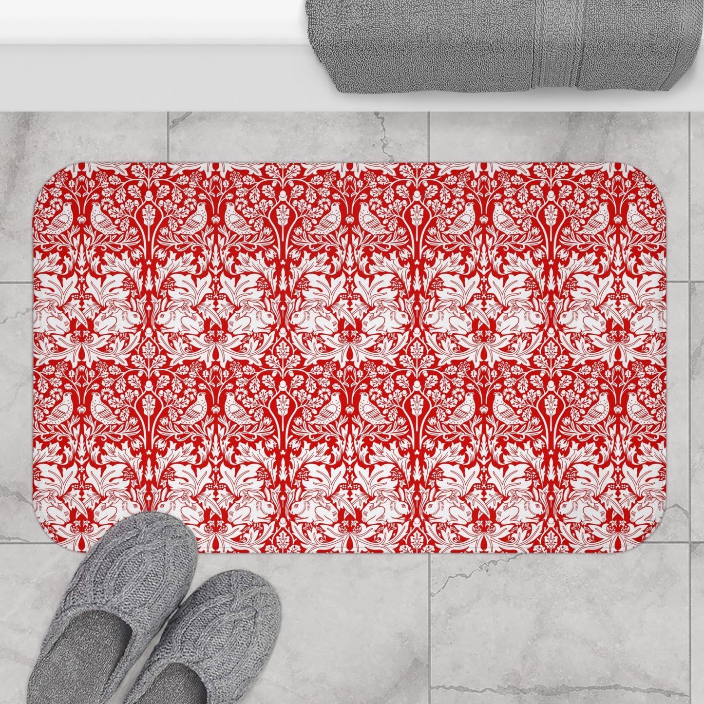 Red and white patterned bath mat on a tiled floor with gray slippers and towel.
