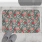 Floral patterned bath mat on a tiled floor with slippers and a towel.