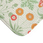 A rectangular microfibre bath mat with a floral pattern inspired by William Morris, featuring colours predominantly in green and orange.