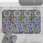 Floral patterned bath mat on a tiled floor with slippers and a towel.