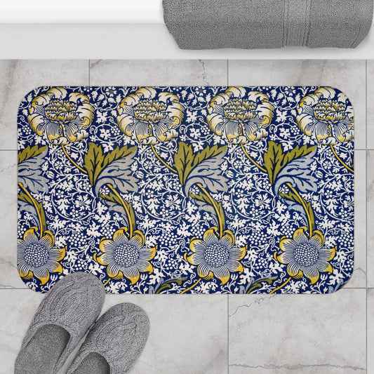 Floral patterned bath mat on a tiled floor with slippers and a towel.