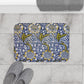 Decorative bath mat with floral pattern on a tiled floor, next to slippers and a towel.