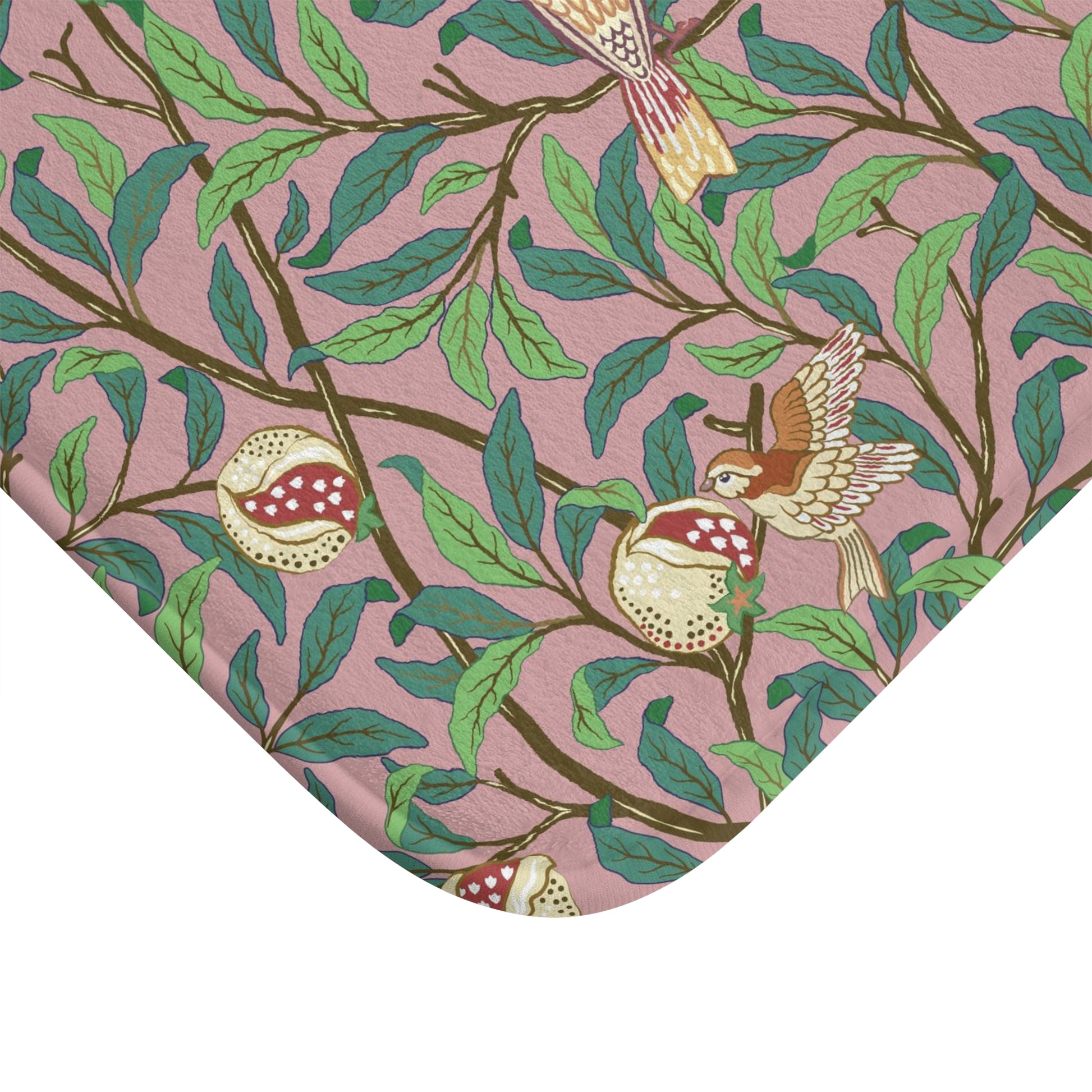A rectangular microfibre bath mat with a William Morris floral pattern featuring birds and pomegranates in pink, green and white colours.