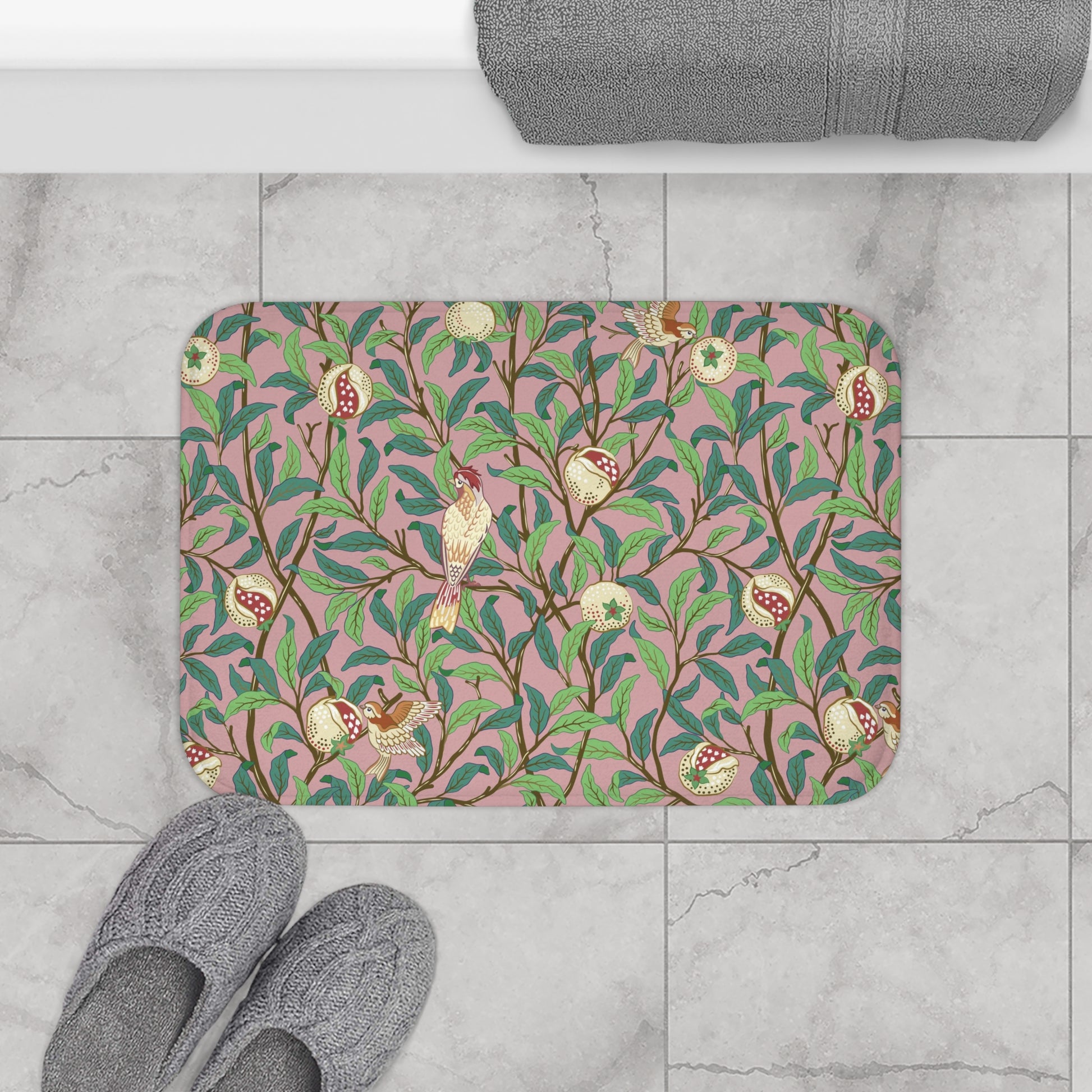 A rectangular microfibre bath mat with a William Morris floral pattern featuring birds and pomegranates in pink, green and white colours.