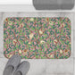 A rectangular microfibre bath mat with a William Morris floral pattern featuring birds and pomegranates in pink, green and white colours.