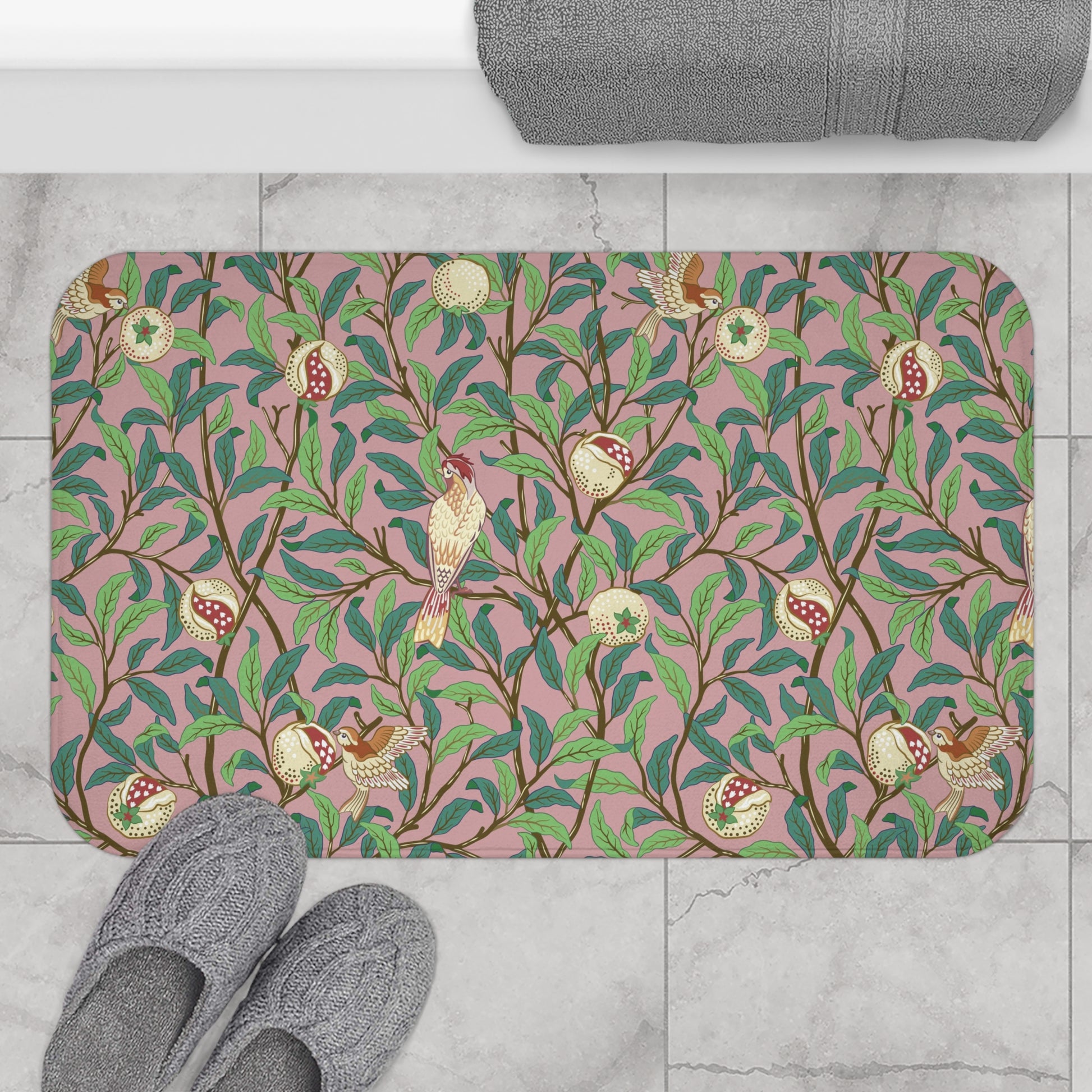 A rectangular microfibre bath mat with a William Morris floral pattern featuring birds and pomegranates in pink, green and white colours.