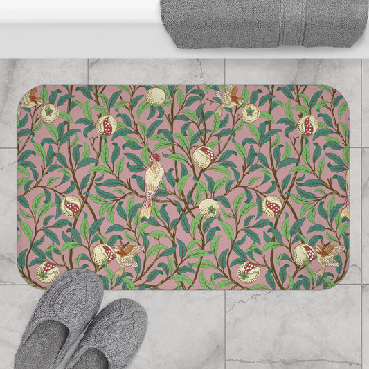 A rectangular microfibre bath mat with a William Morris floral pattern featuring birds and pomegranates in pink, green and white colours.